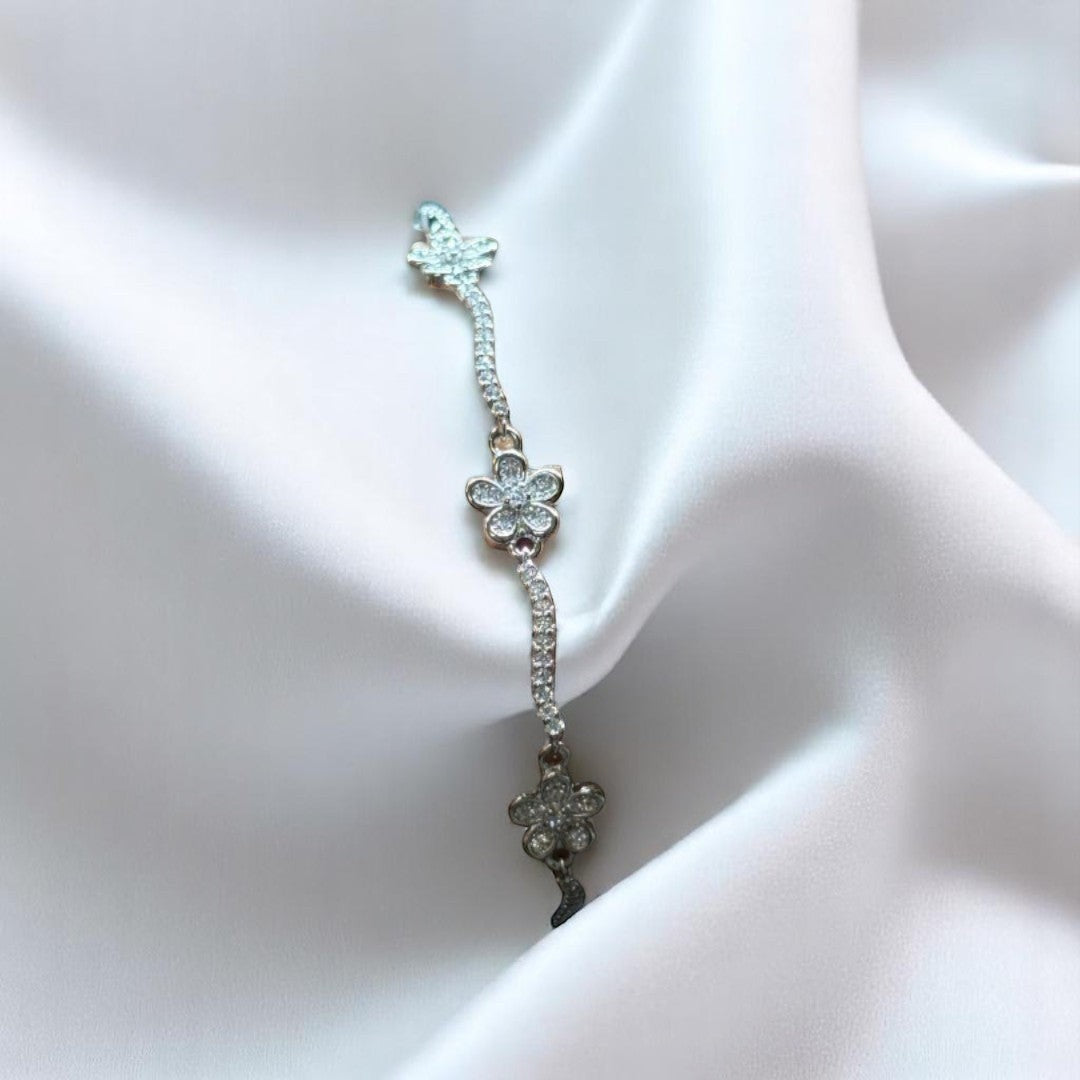 BlingbyAnvika 925 sterling silver bracelet featuring delicate flower charms with sparkling stones on white silk fabric.