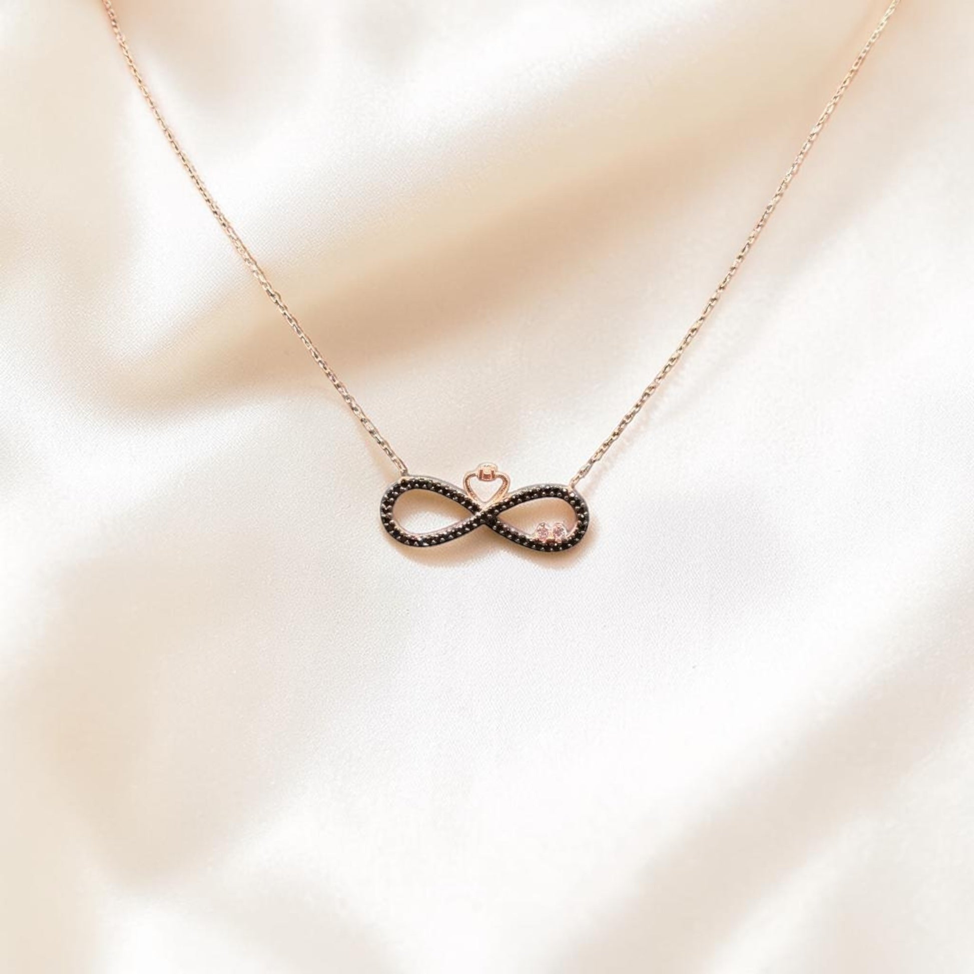 BlingbyAnvika rose gold plated 925 sterling silver infinity necklace with a small heart detail on a white fabric