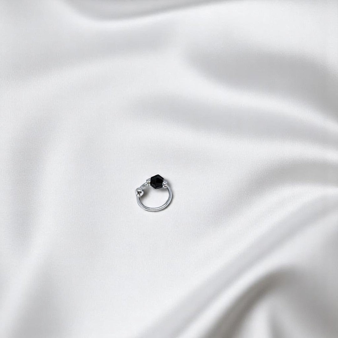 BlingbyAnvika 925 sterling silver nose ring featuring a small black bead on a white satin background.
