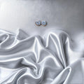 BlingbyAnvika 925 silver round blue gemstone stud earrings with polished bezel, set against a silver satin background.