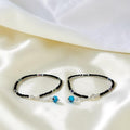 BlingbyAnvika 925 sterling silver evil eye anklets with black beaded thread on a soft white satin background.