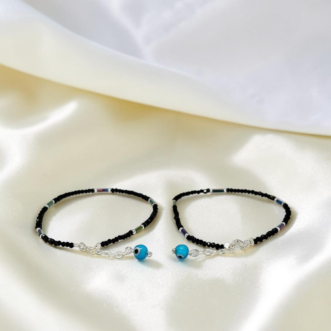 BlingbyAnvika 925 sterling silver evil eye anklets with black beaded thread on a soft white satin background.