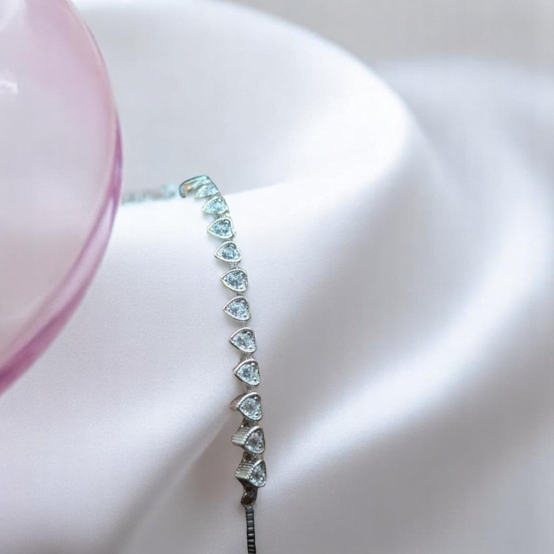 BlingbyAnvika 925 sterling silver bracelet with a row of small, sparkling heart-shaped stones on a white satin background.