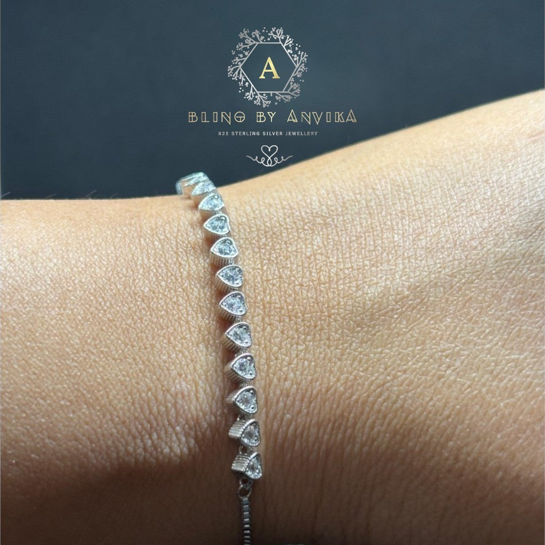 BlingbyAnvika 925 sterling silver bracelet with a row of small, sparkling heart-shaped stones on a white satin background.
