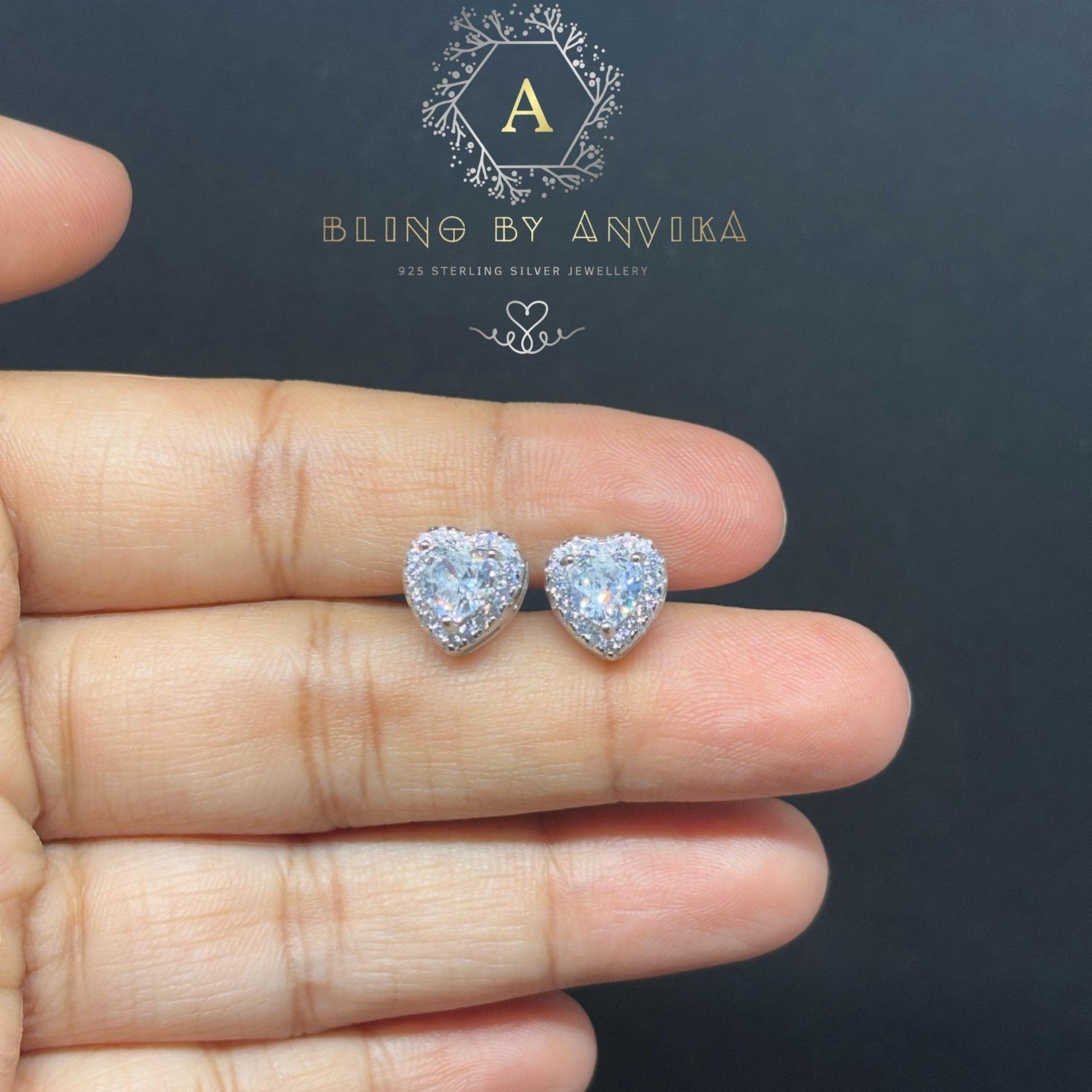 BlingbyAnvika heart-shaped sterling silver stud earrings featuring sparkling AAA-grade zircon stones on a hand.