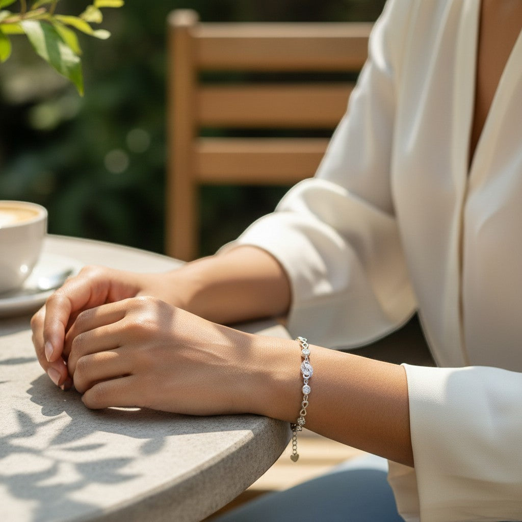 BlingbyAnvika 925 silver infinity link chain bracelet with sparkling accents worn on a woman's wrist at a cafe table.