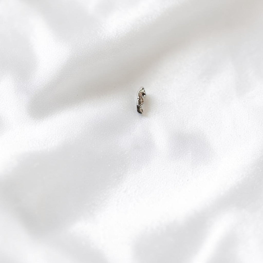 BlingbyAnvika 925 sterling silver seahorse nose pin with intricate detailing on a grey concrete surface.