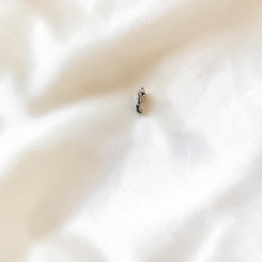 BlingbyAnvika 925 sterling silver seahorse nose pin with intricate detailing on a grey concrete surface.