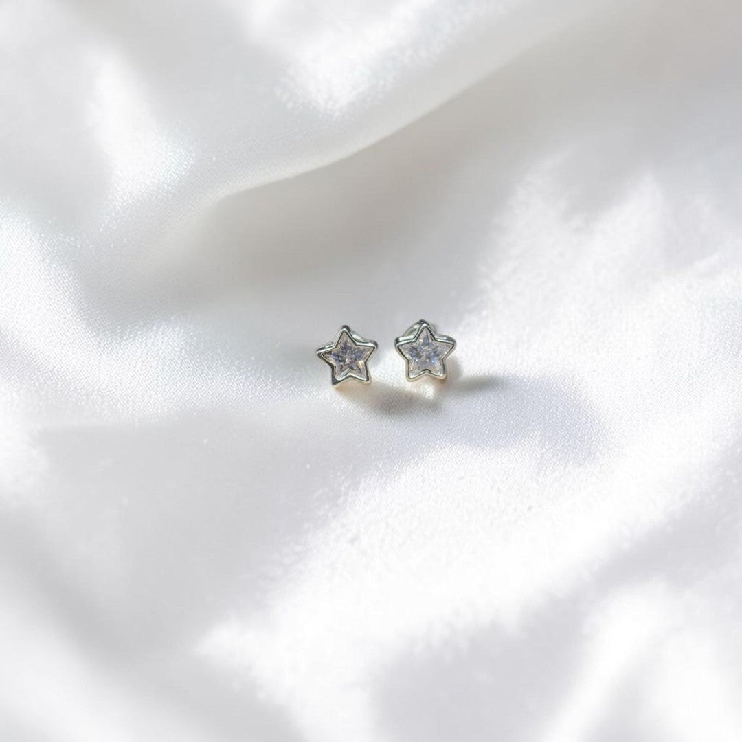 BlingbyAnvika sterling silver star stud earrings featuring sparkling AAA-grade zircon stones on white satin fabric.