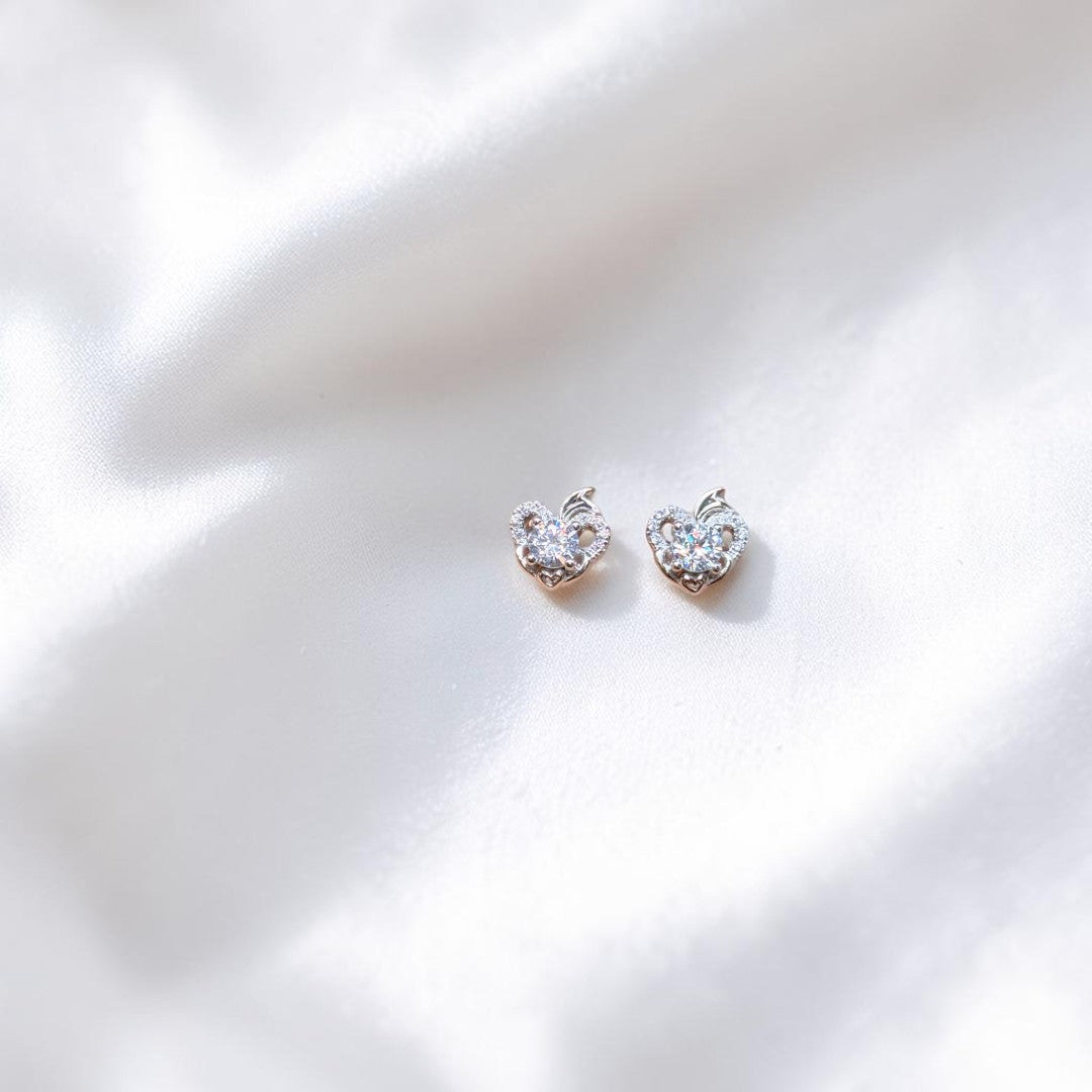 BlingbyAnvika sterling silver heart-shaped stud earrings featuring sparkling AAA-grade zircon stones on white fabric.