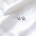 BlingbyAnvika sterling silver heart-shaped stud earrings with sparkling AAA-grade zircon stones on white silk fabric.