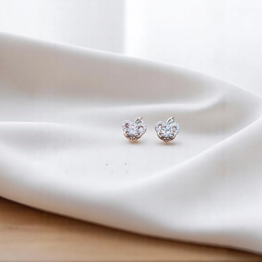BlingbyAnvika sterling silver heart-shaped stud earrings featuring sparkling AAA-grade zircon stones on white fabric.