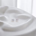 BlingbyAnvika square sterling silver stud earrings with sparkling AAA-grade zircon stones on white silk fabric.