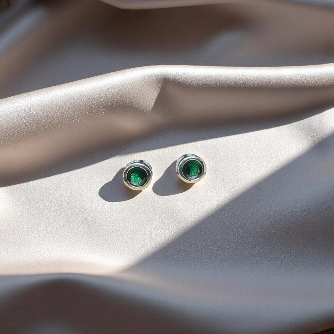 BlingbyAnvika sterling silver stud earrings featuring vibrant round green stones on a soft champagne satin background.