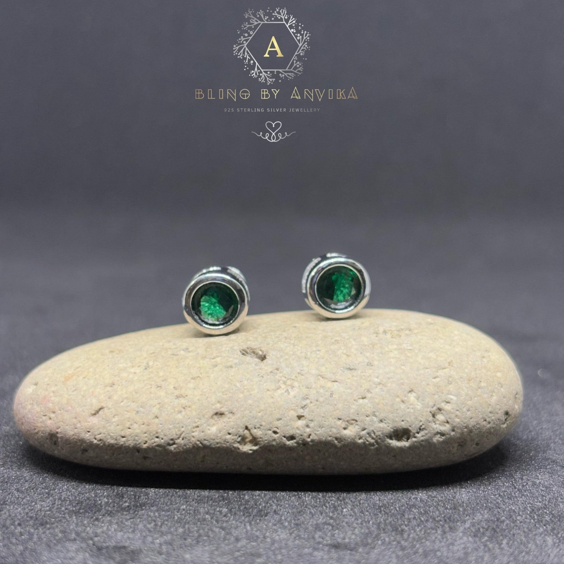 BlingbyAnvika sterling silver stud earrings featuring vibrant green stones on a smooth stone surface