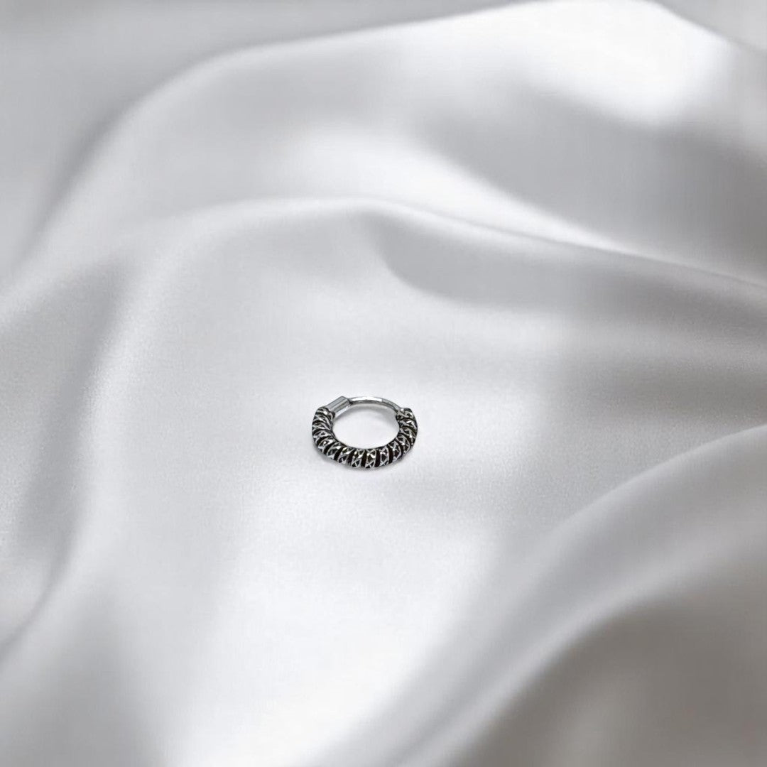 BlingbyAnvika 925 sterling silver nose ring with a twisted rope texture design on a soft white satin background.