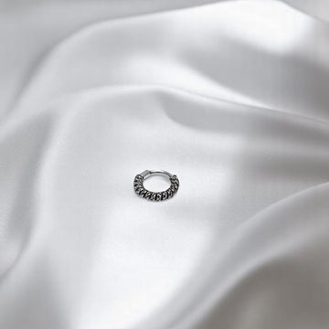 BlingbyAnvika 925 sterling silver nose ring with a twisted rope texture design on a soft white satin background.